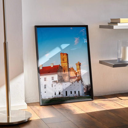 Elegant building architecture wall art poster with blue sky and warm sunlight in black frame leaning on floor.