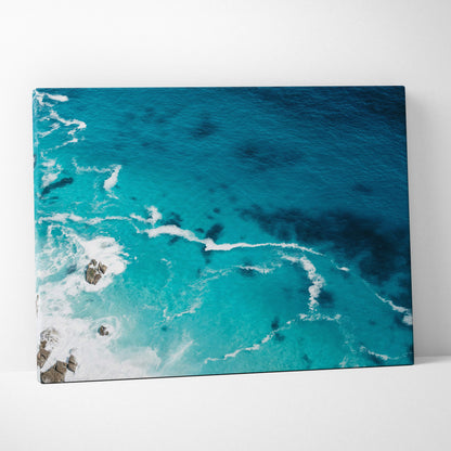 A vibrant turquoise ocean canvas wall art print featuring crashing waves and rocky outcrops for coastal decor