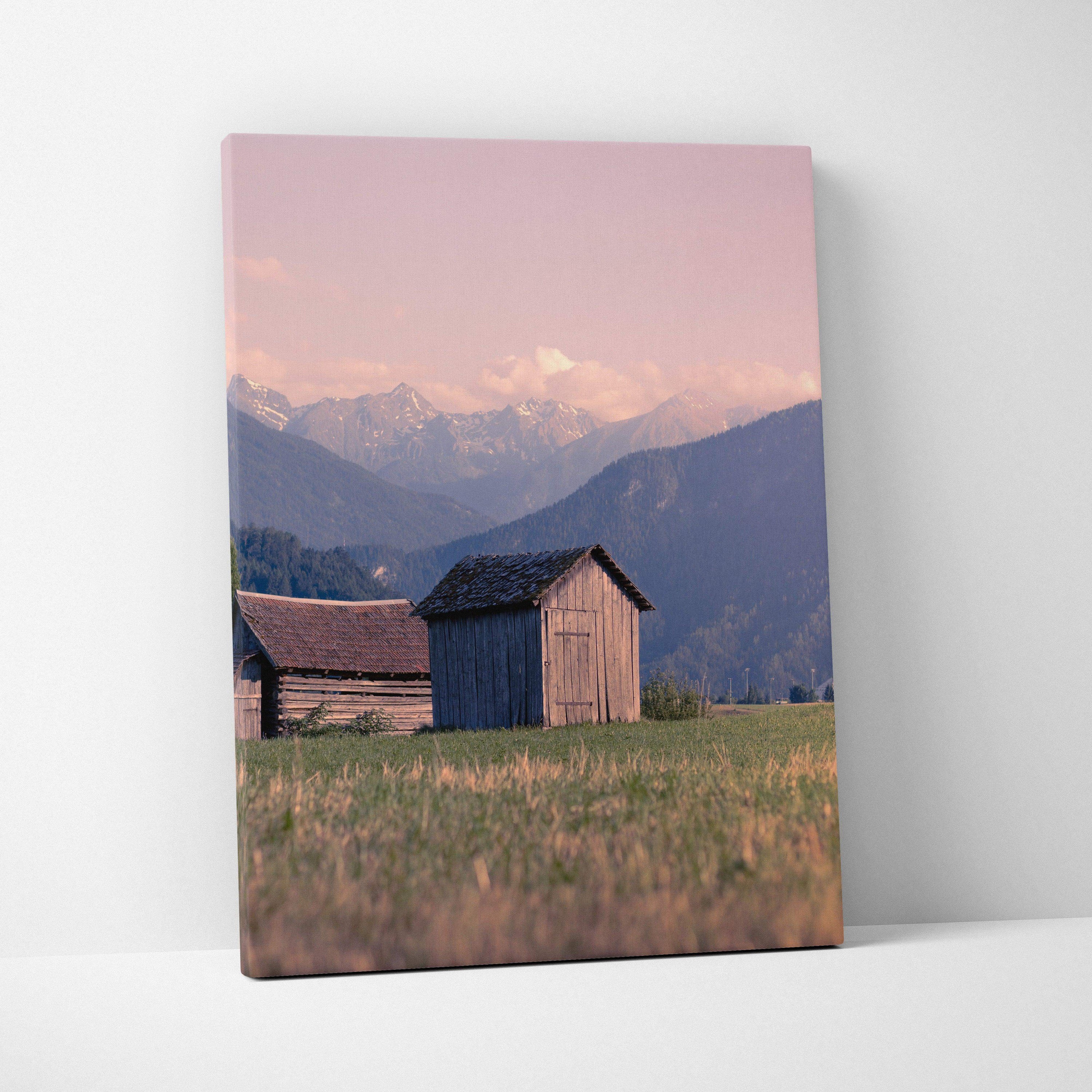 Canvas wall art featuring rustic wooden buildings with mountains and a pink sunset sky background.