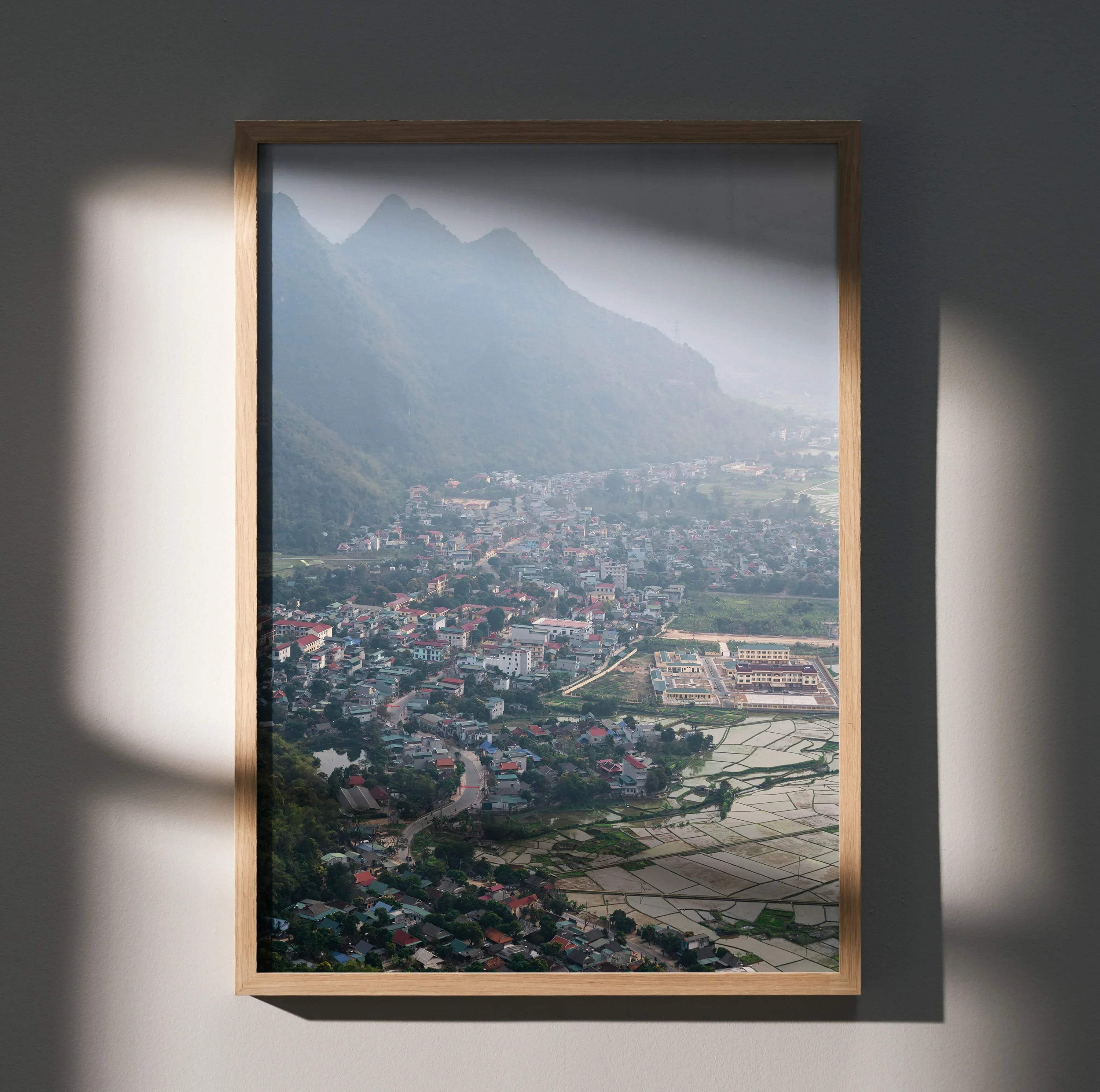 Vertical urban cityscape poster with misty mountains and town, framed wall art print.