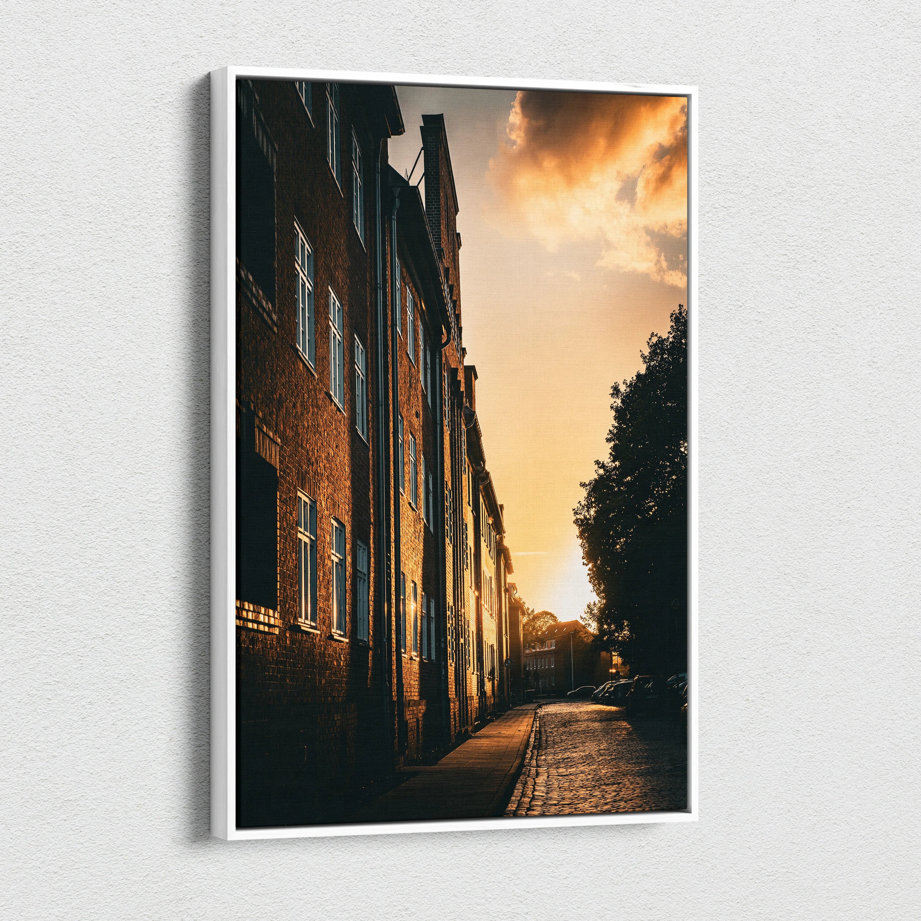 Vertical canvas wall art featuring a city skyline at sunset with golden light on brick buildings.