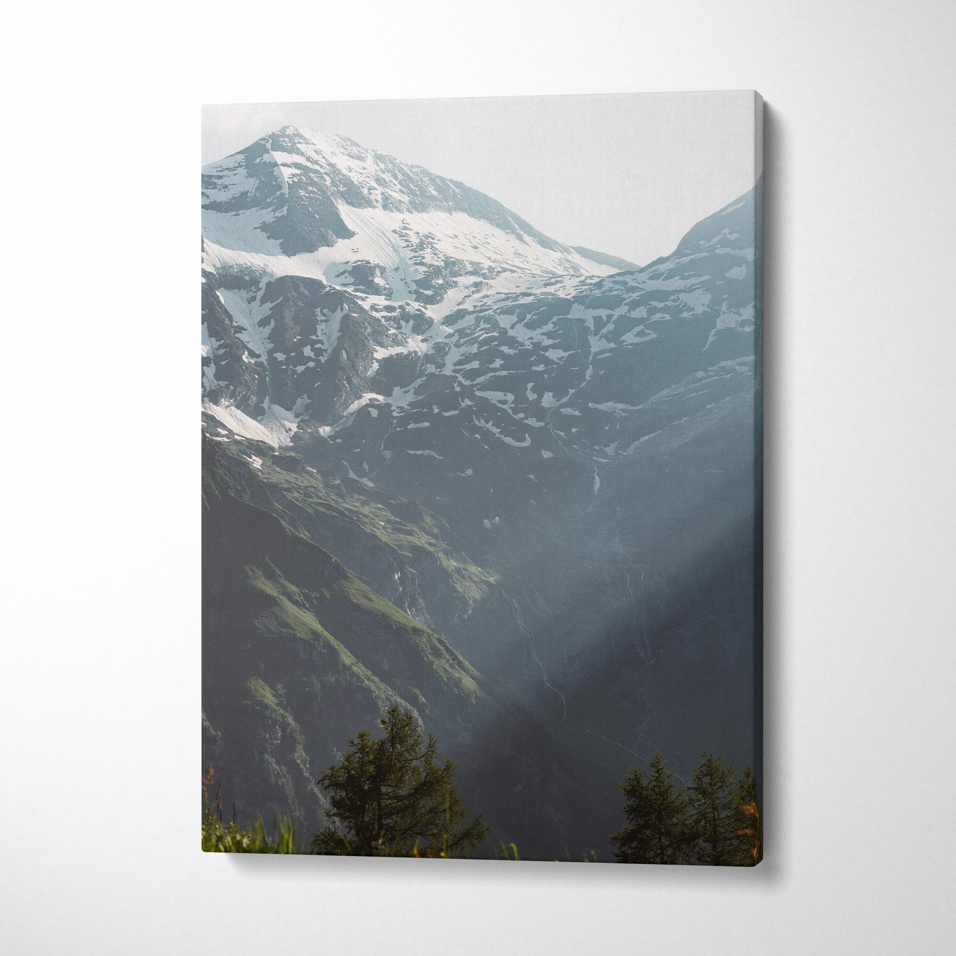 Vertical canvas wall art featuring snowy mountain peaks with dark forested slopes and soft natural light rays.