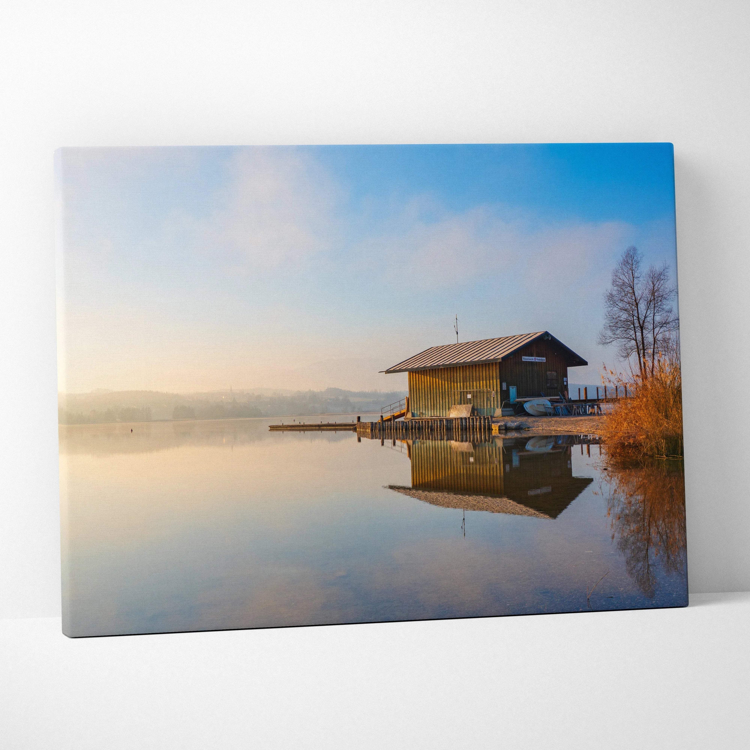 Canvas wall art featuring a serene lakeside cabin reflected in calm water at sunrise.