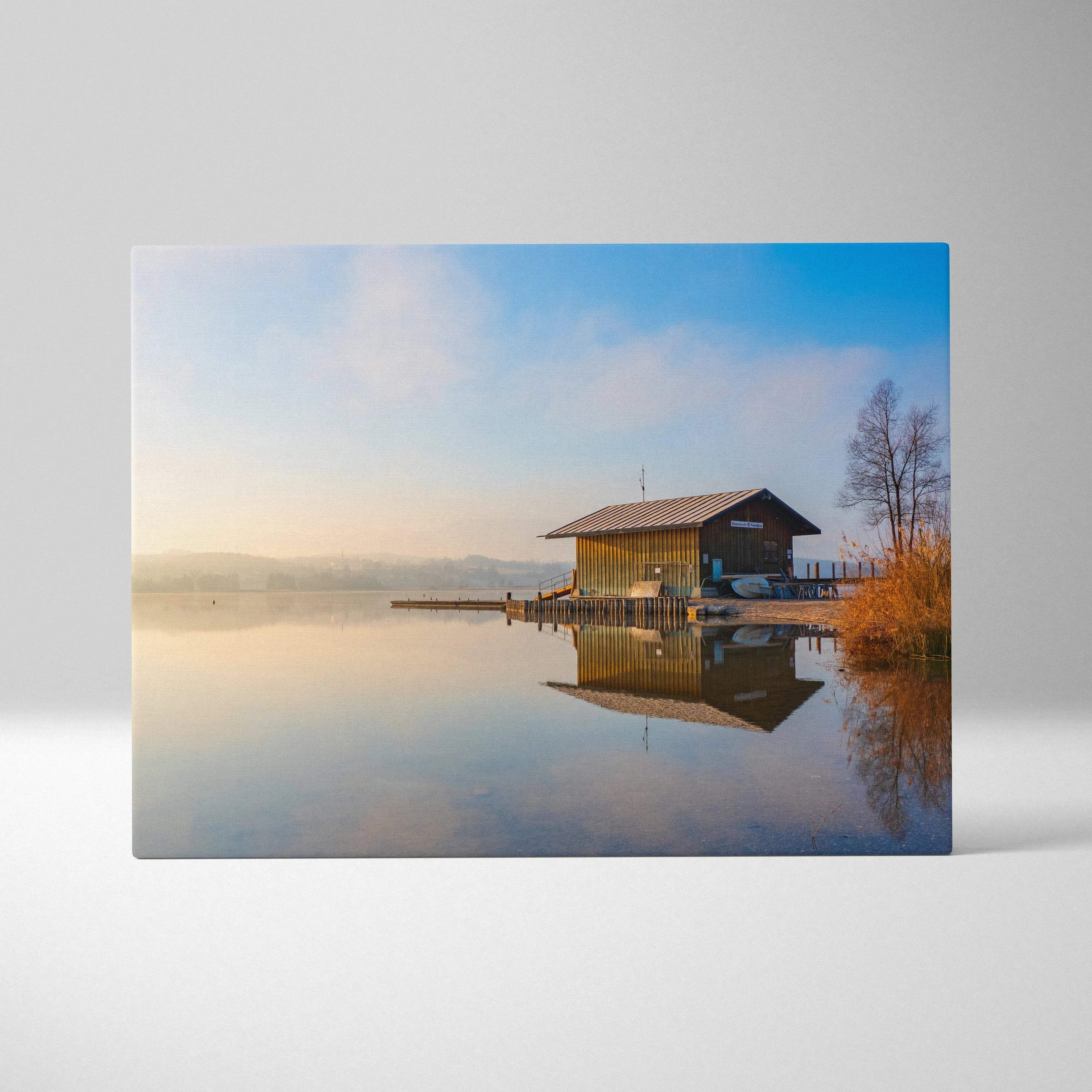 Canvas wall art depicting a serene lakeside building reflecting on calm water under a soft blue sky.