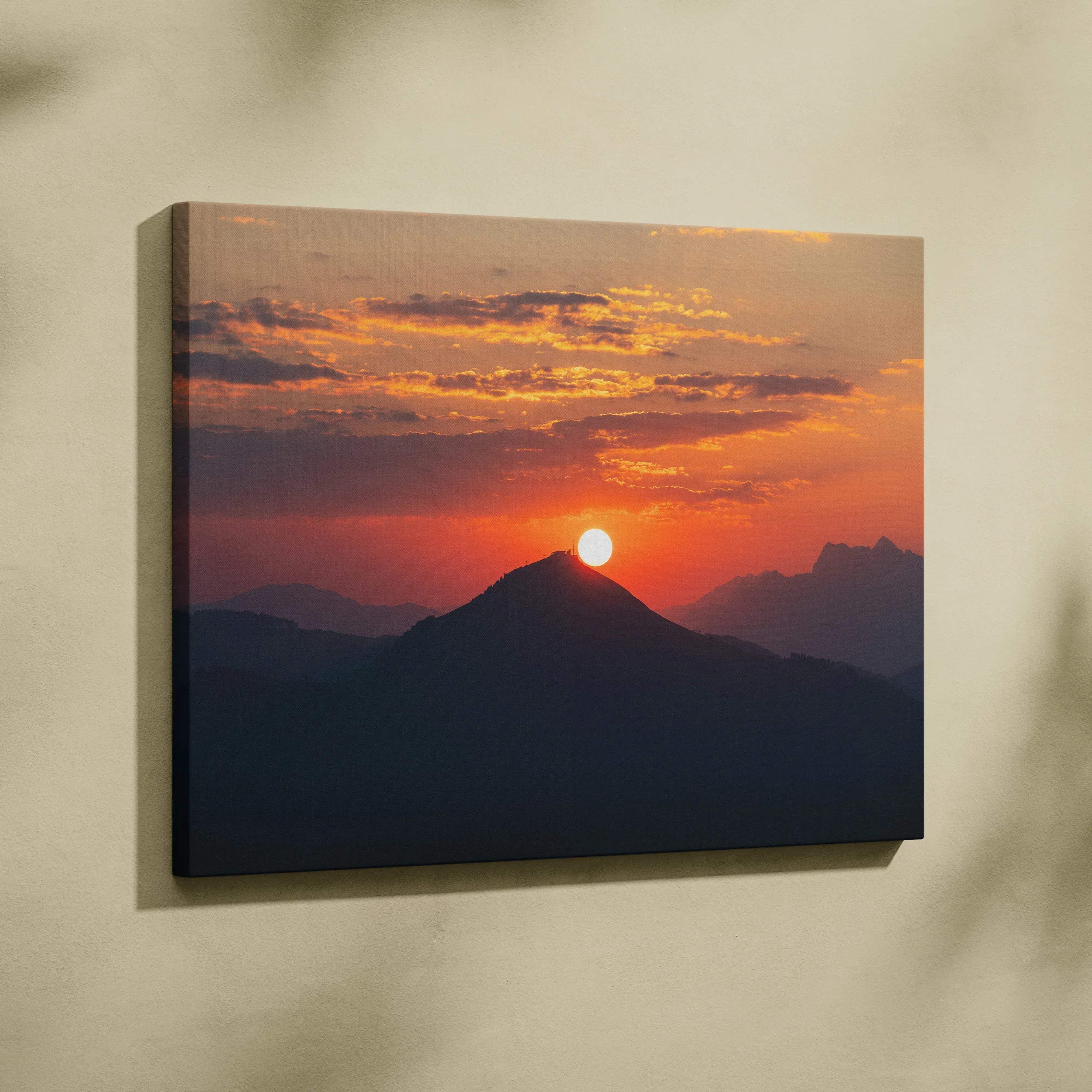 A rectangular canvas wall art featuring a vibrant sunset over mountain peaks in warm orange and red hues