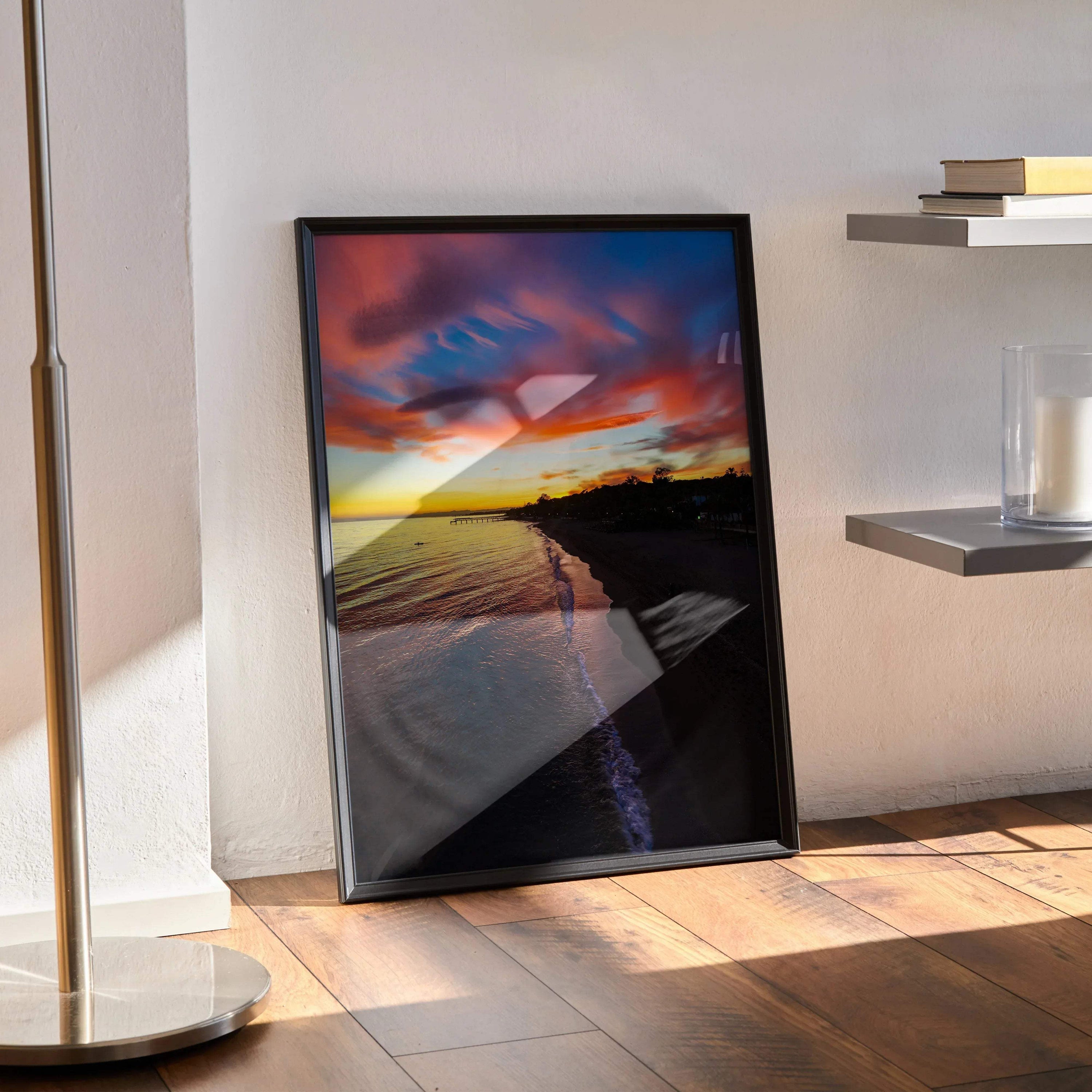 Vibrant beach sunset poster with colorful sky and calm ocean, framed wall art leaning on floor.