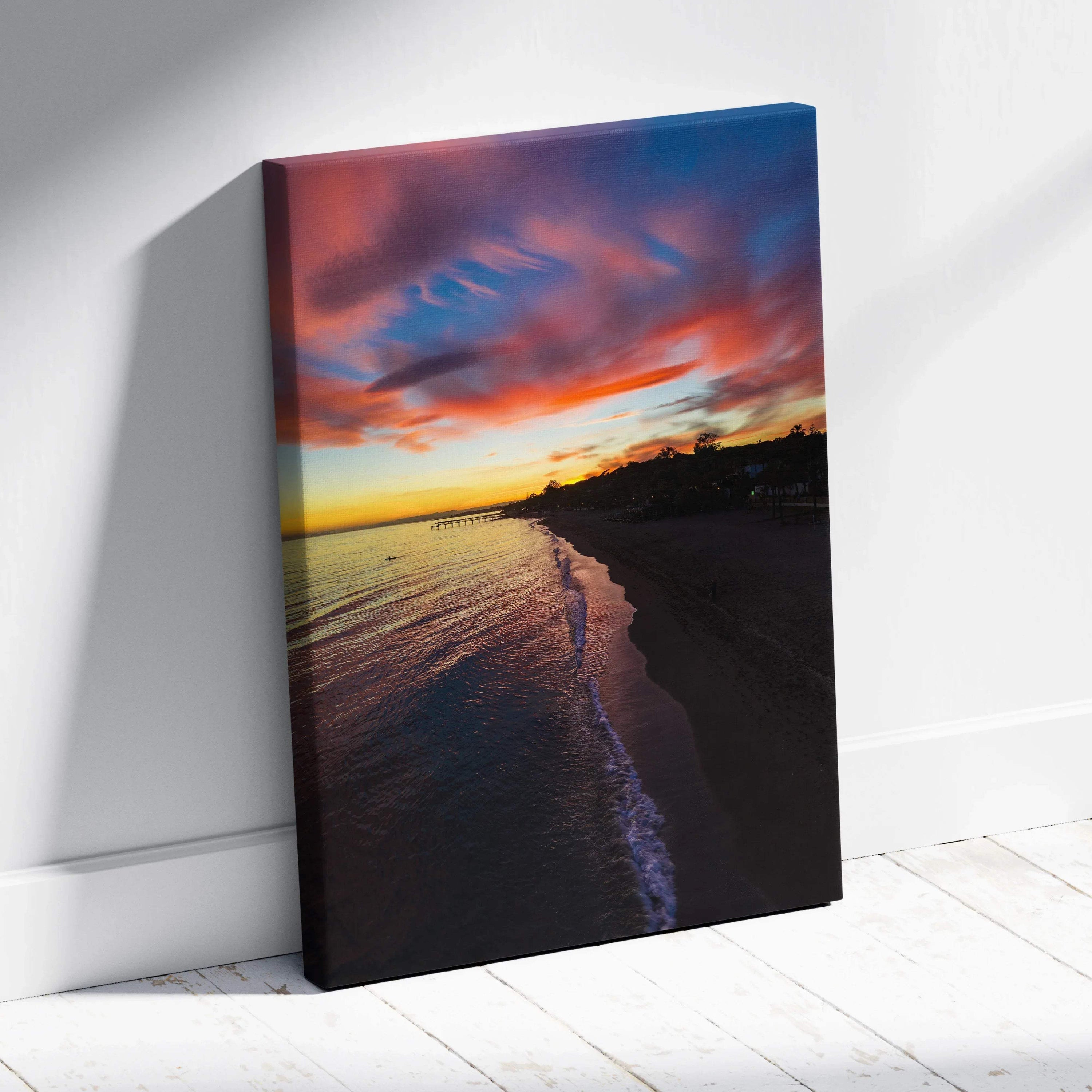 Vibrant beach sunset canvas wall art with colorful sky and dark shoreline silhouette.