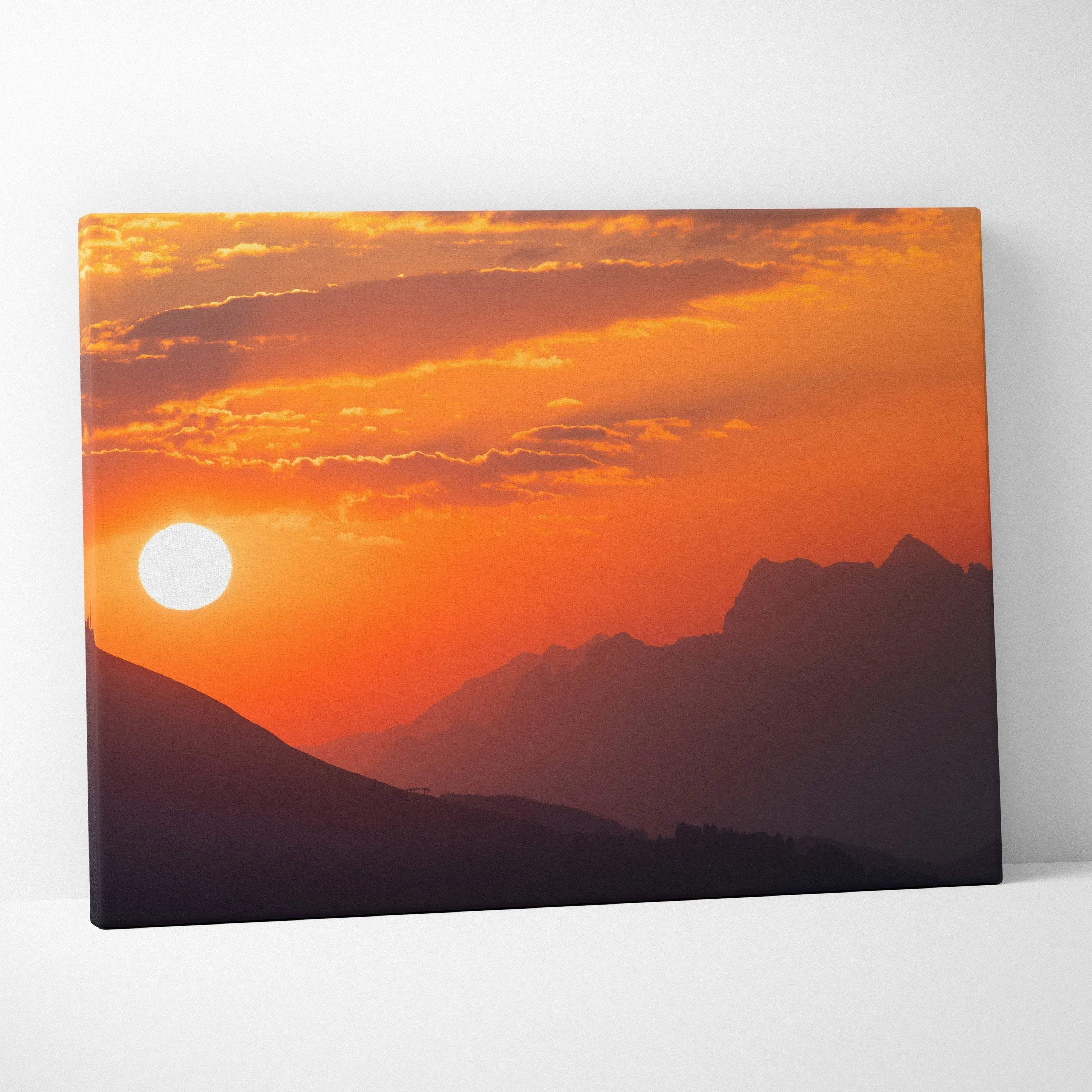 Canvas wall art featuring a vibrant orange and red mountain sunset with silhouetted peaks and glowing sun.