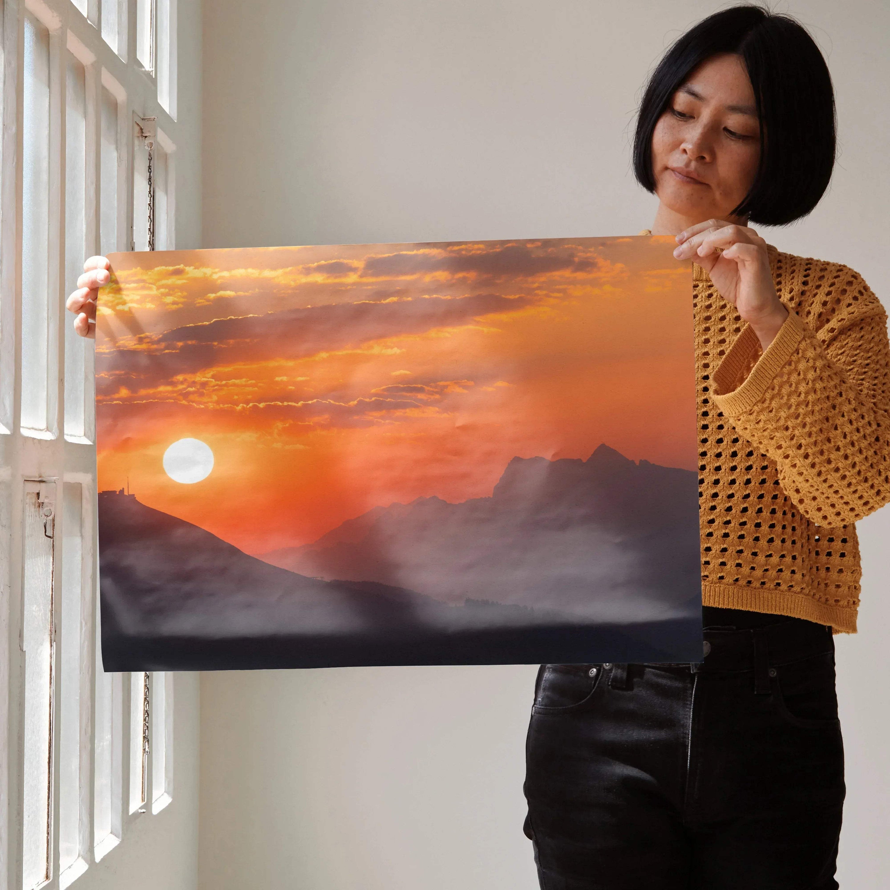Woman holding a vibrant mountain sunset poster with orange and purple hues, wall art for decor.