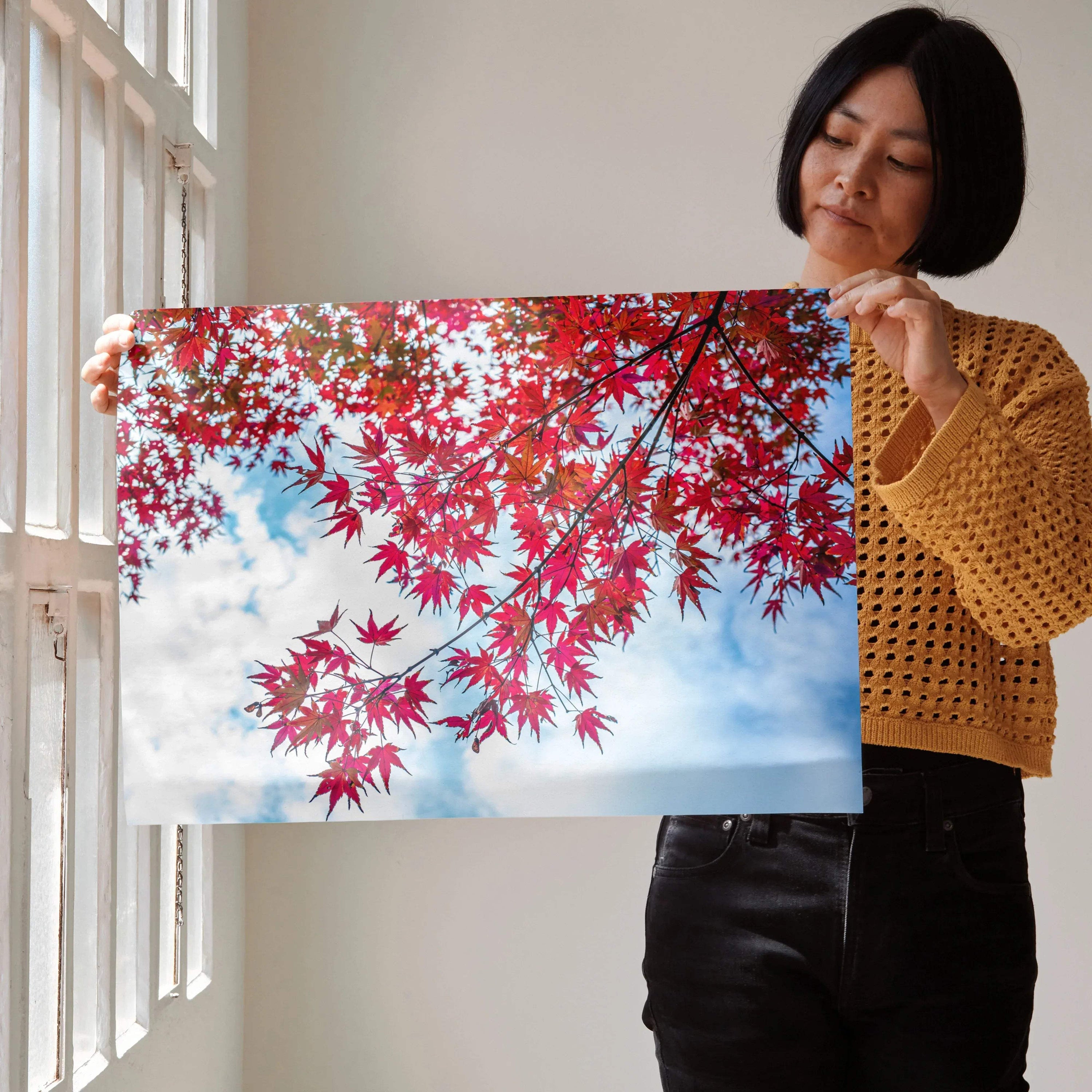 Vibrant autumn leaves with red foliage and blue sky background poster wall art held by woman.