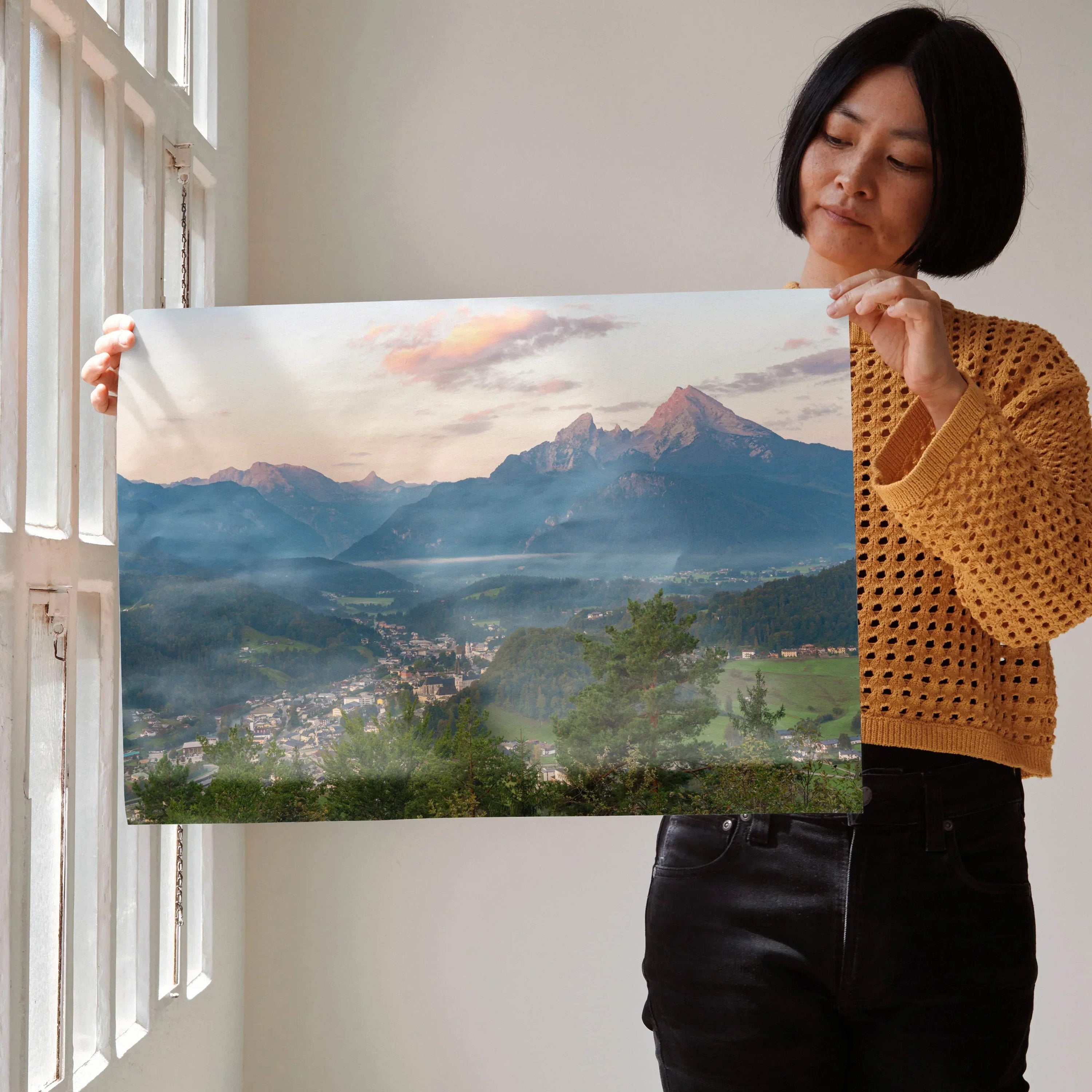 Mountain sunset wall art poster with vibrant orange and pink sky over misty peaks and village below.
