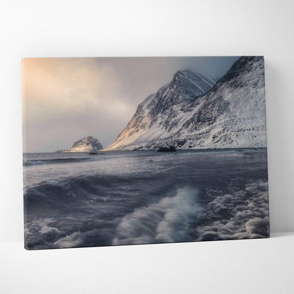 Canvas wall art featuring snow-covered mountains with moody skies and turbulent ocean waves at sunset.