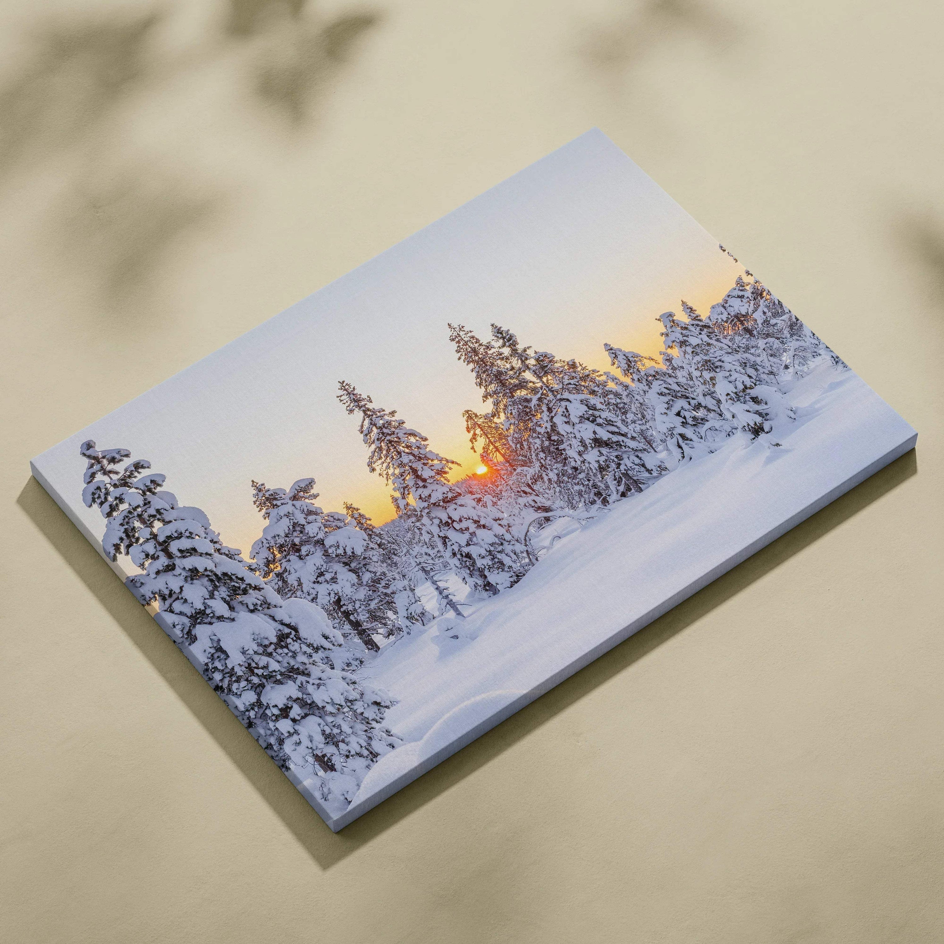 Canvas wall art featuring a snowy forest at sunset with warm orange and purple sky hues.