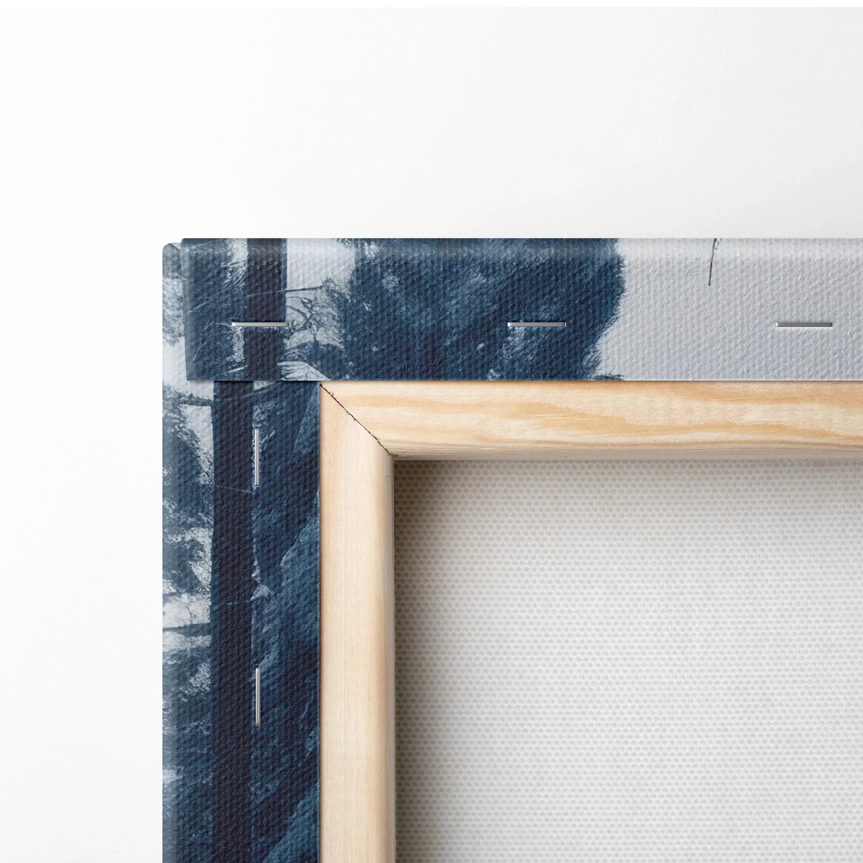 Close-up of wooden frame and stretched canvas showing snowy river and dark blue forest scene on winter landscape wall art.