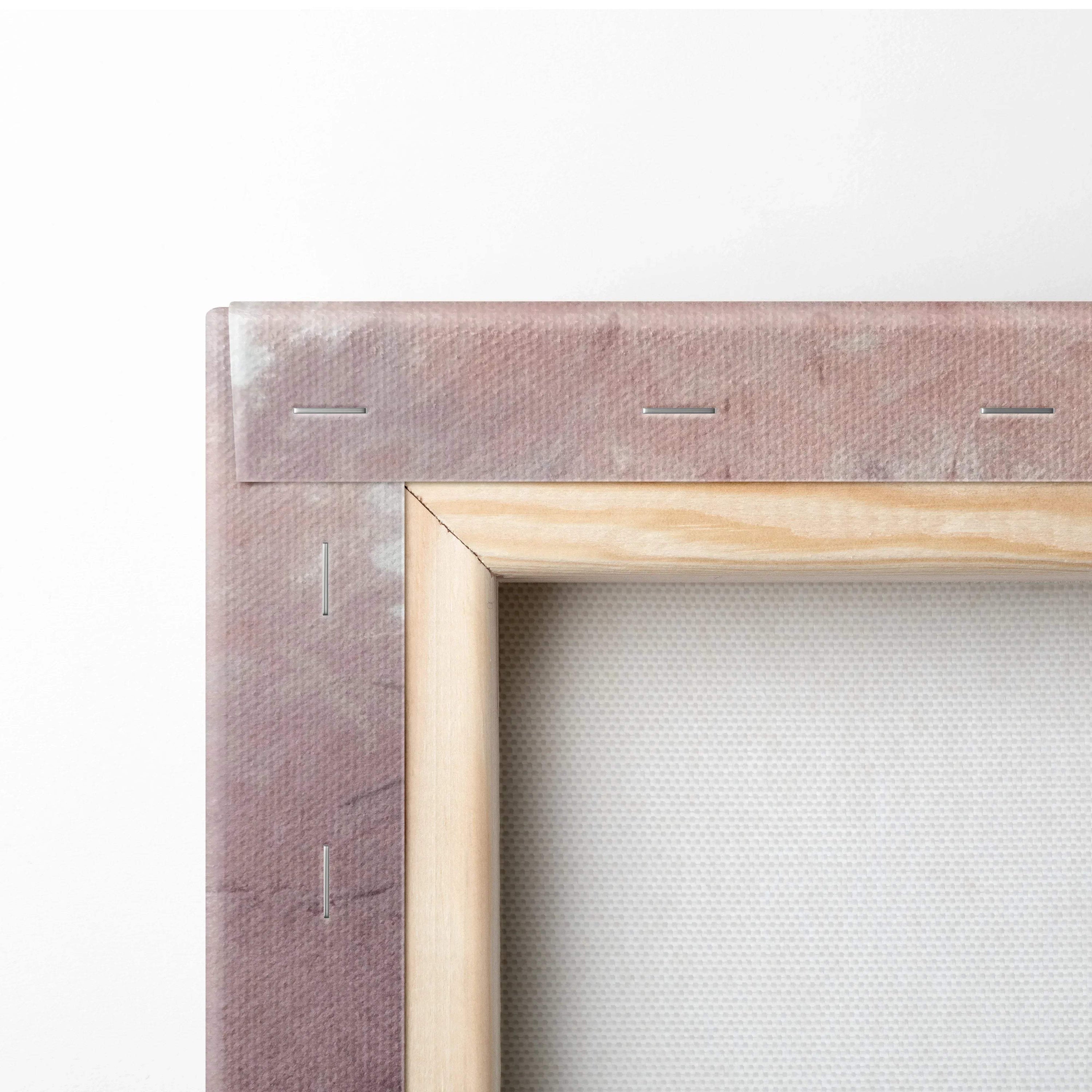Close-up of wooden frame and stapled edge of a wrapped canvas print with light pink and beige tones.
