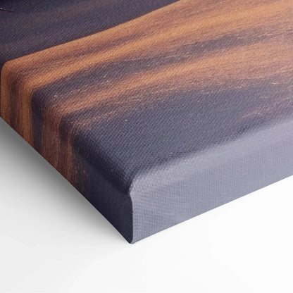 Close-up of textured canvas art print with warm orange and dark purple winter sunset colors wrapped on wooden frame.