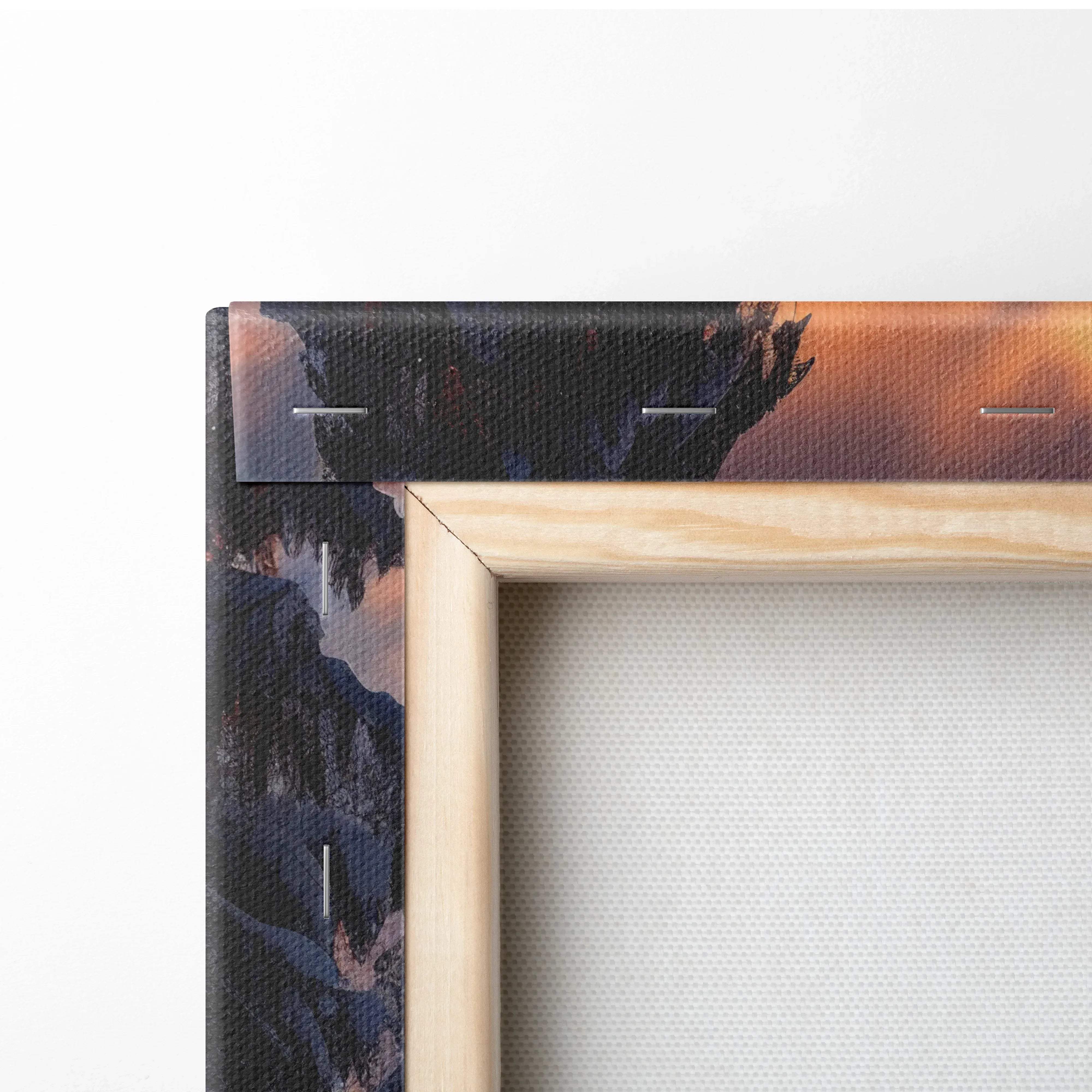 Light-colored wooden frame holding a canvas print of a dark mountain landscape under an orange and purple sky