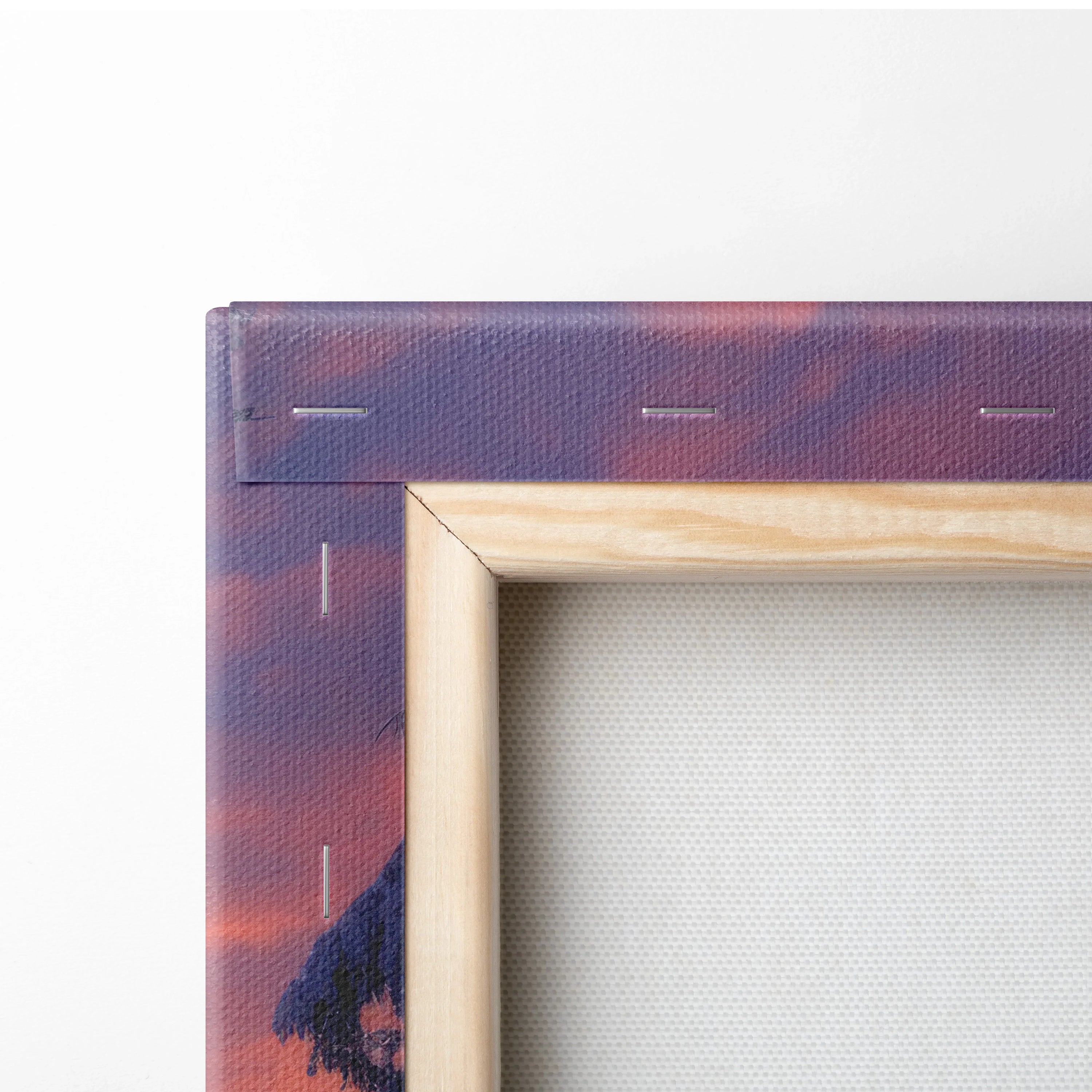 Close-up of wooden-framed canvas wall art with purple and orange snowy sunset print and visible staple edges.