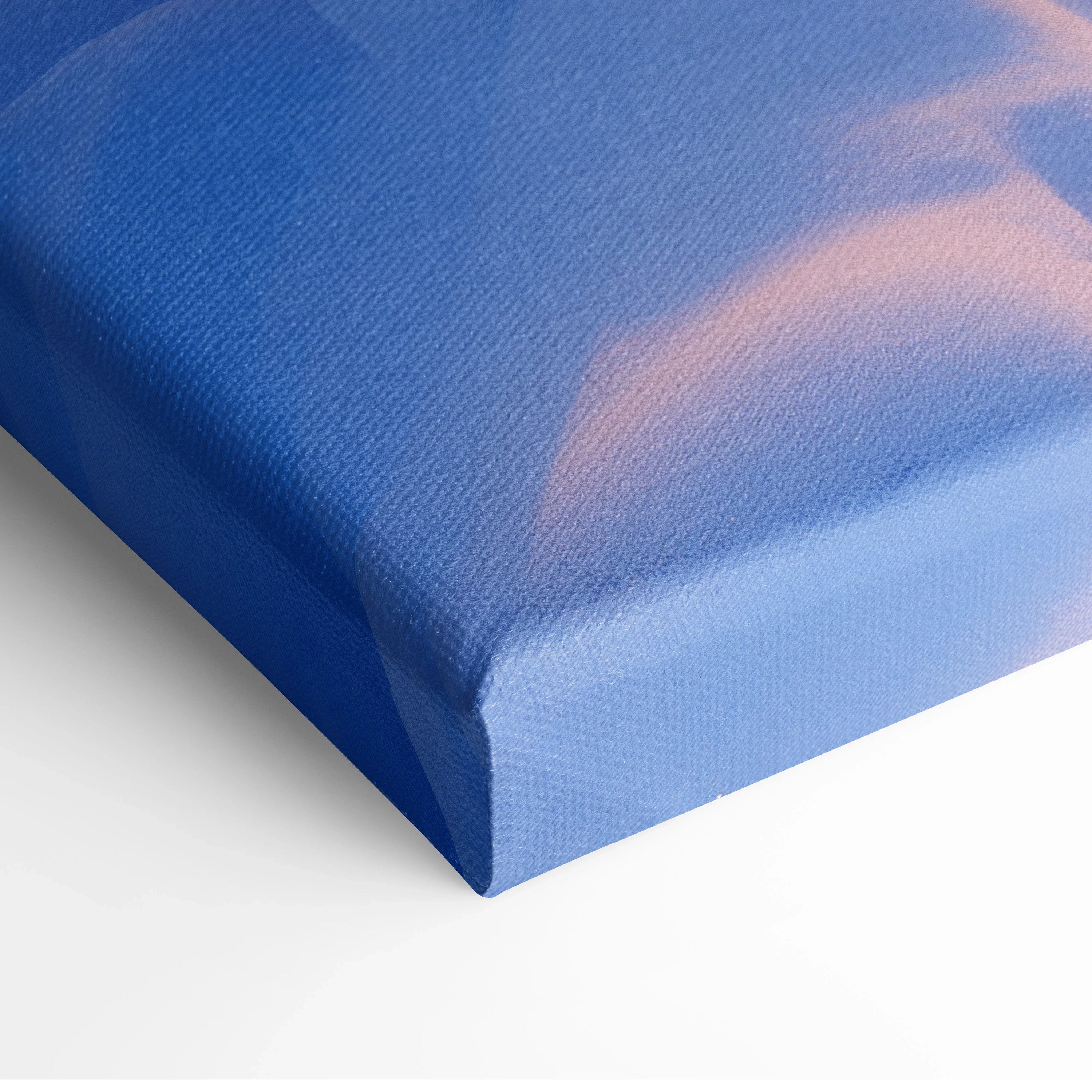 Close-up of canvas wall art corner depicting a blue and orange snowy sunset scene with textured fabric surface.