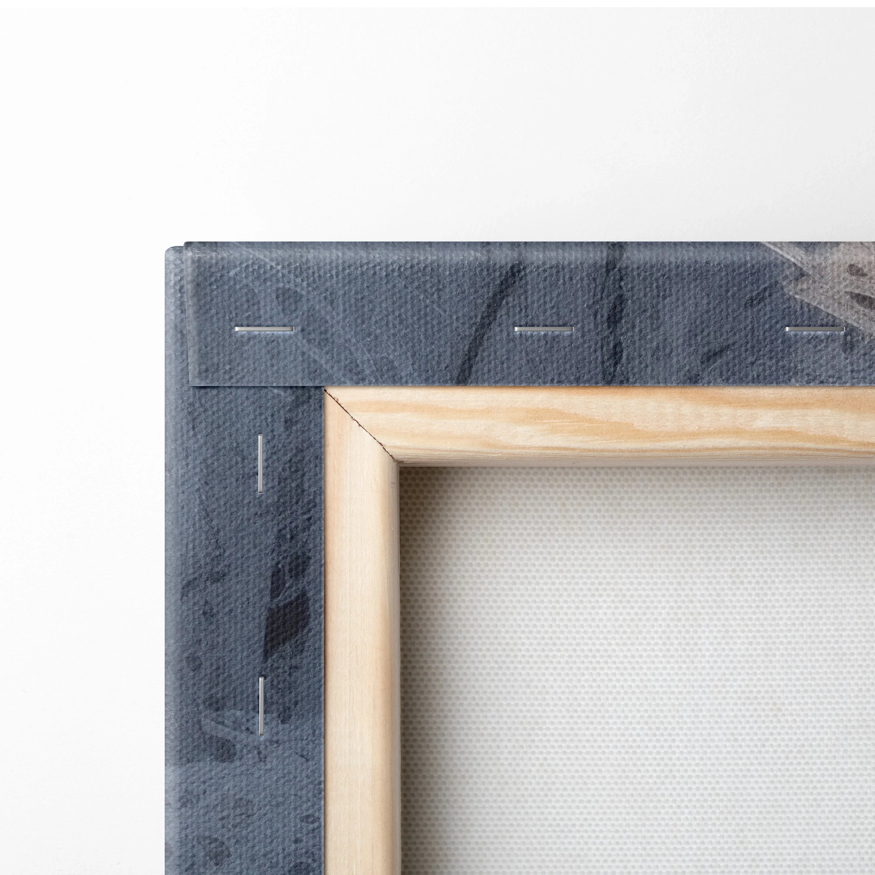 Close-up of wooden frame corner with dark blue canvas stretched and stapled, textured fabric visible on back of wall art.